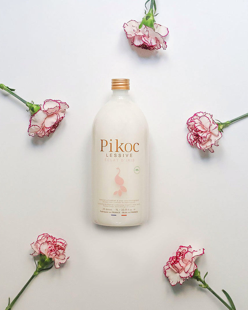 Pikoc Éclat d’Iris vaskemiddel omgivet af lyserøde blomster